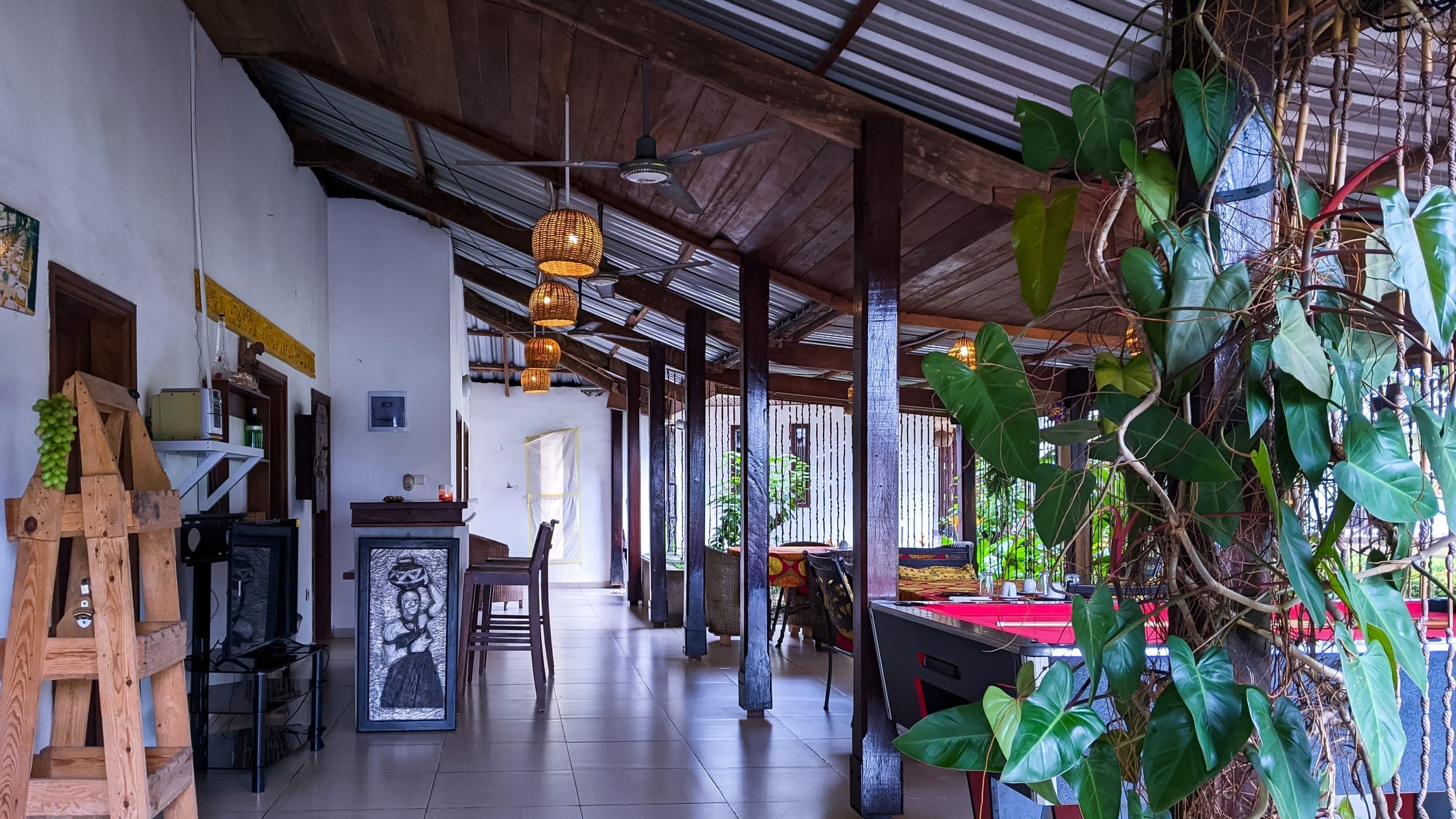 The veranda's lounge corridor, with the pool table, wicker furniture and lush plants
