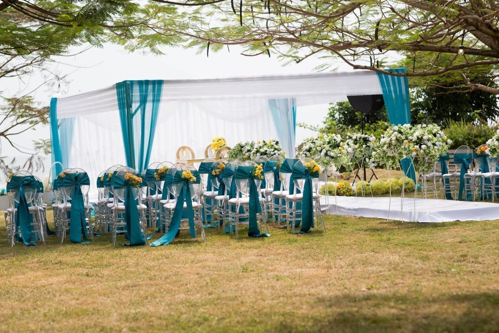 Ceremony chairs dressed in teal beneath the trees, set for a wedding on the lawn